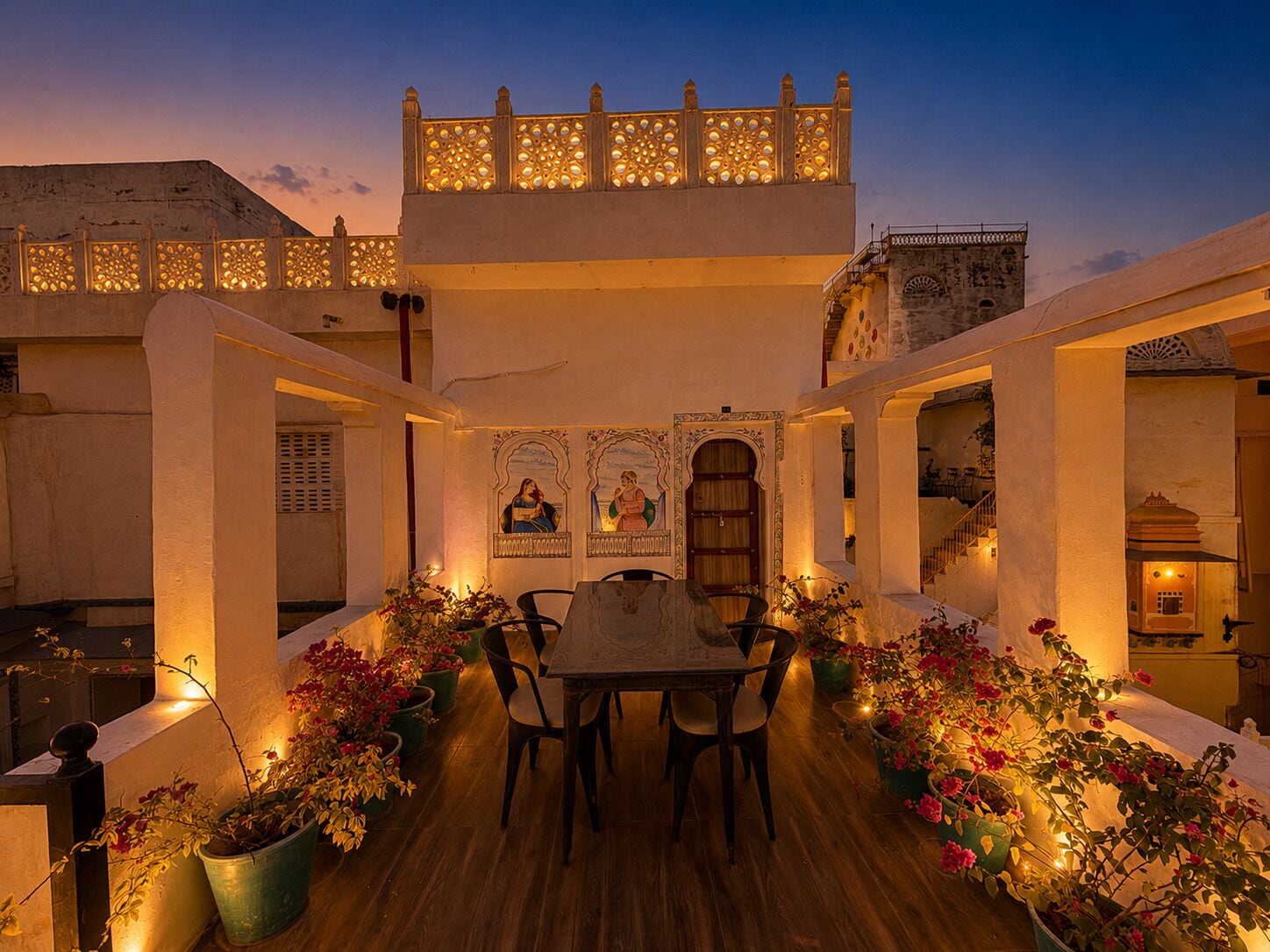 A courtyard with a dining table and chairs, surrounded by potted plants and decorative elements.
