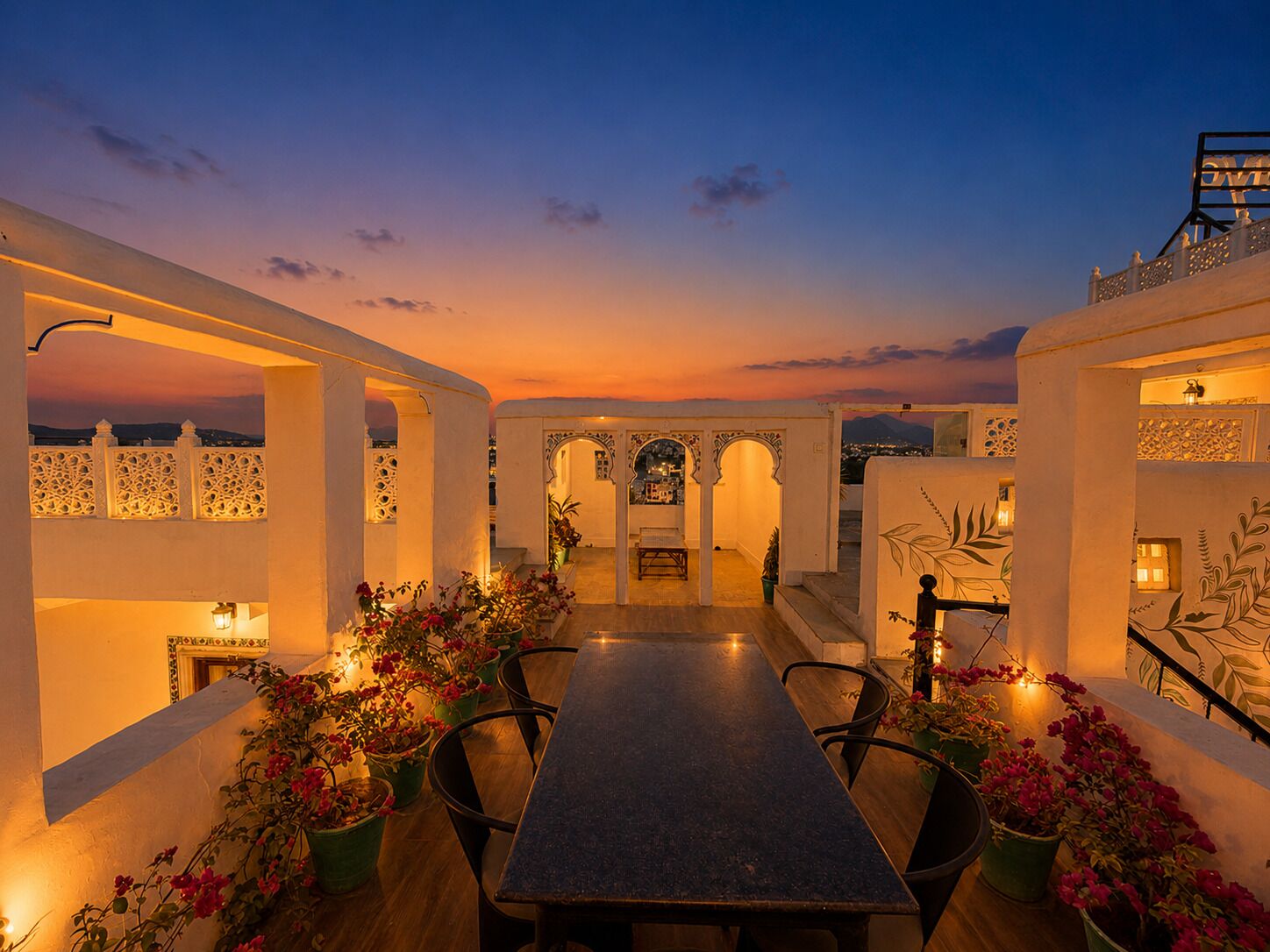 A rooftop terrace with a long table, chairs, and potted plants.