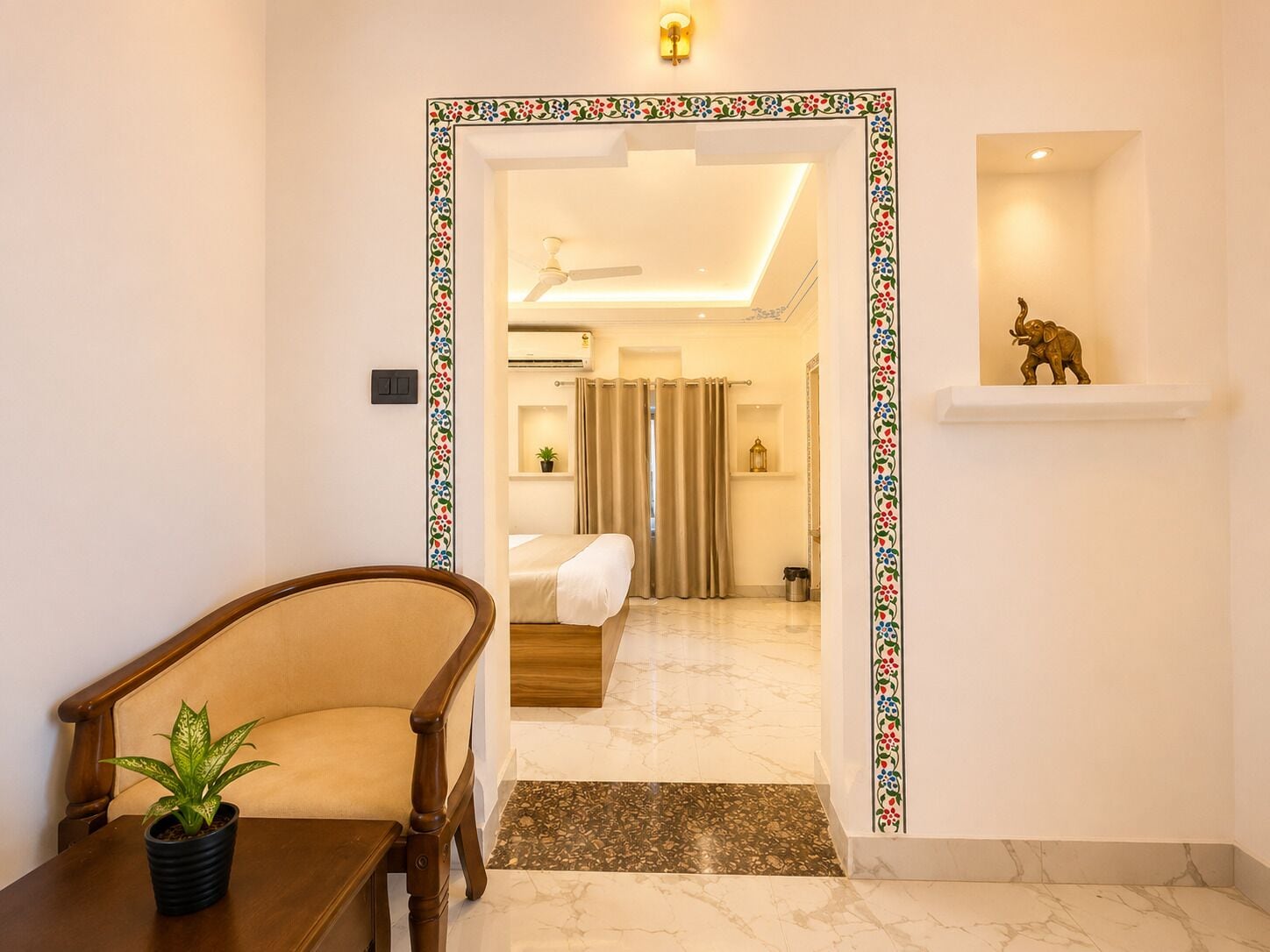 A hotel room with a bed, a ceiling fan, a small shelf with a statue, and a potted plant.