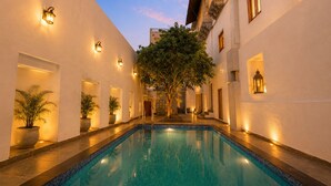 A pool area with a clear blue pool, white walls, and warm lighting. - Amoraya — A Lake View Heritage Haveli (Old City Udaipur) (Udaipur)