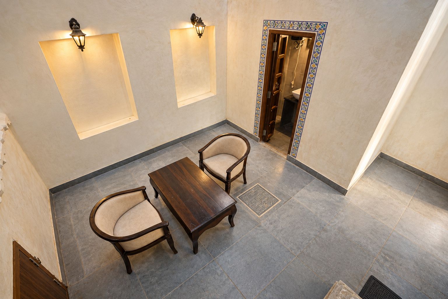 A room with a wooden table and two chairs, a tiled floor, and a wall-mounted light fixture.