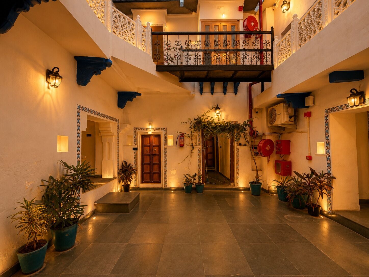 A courtyard with a central staircase, potted plants, and a balcony with ornate railings.