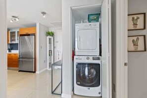 Compact laundry room with a front-loading washer and dryer, a small storage basket, and framed artwork.