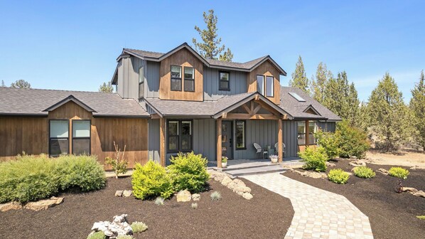 A two-story house with a covered porch, a landscaped garden with various shrubs and rocks, and a paved walkway leading to the entrance.