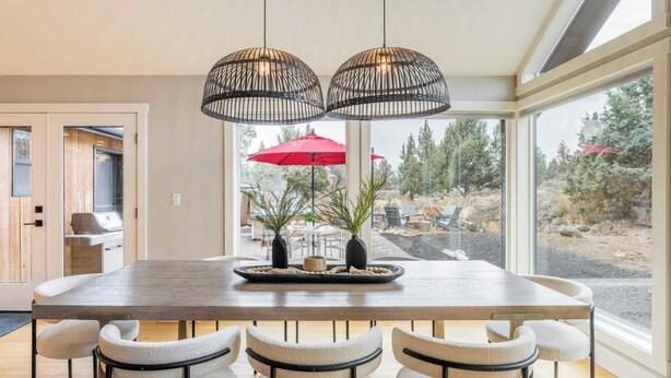 A modern dining area with a large wooden table, four cushioned chairs, and two hanging pendant lights. - The Gem Estate by Avantstay Modern Farmhouse w/ Lavender Fields + Hot Tub (Bend)