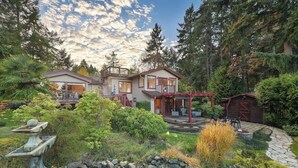 A two-story house with a covered patio and a small pond. - Dolphin House Oceanview Family Getaway (Nanoose Bay)