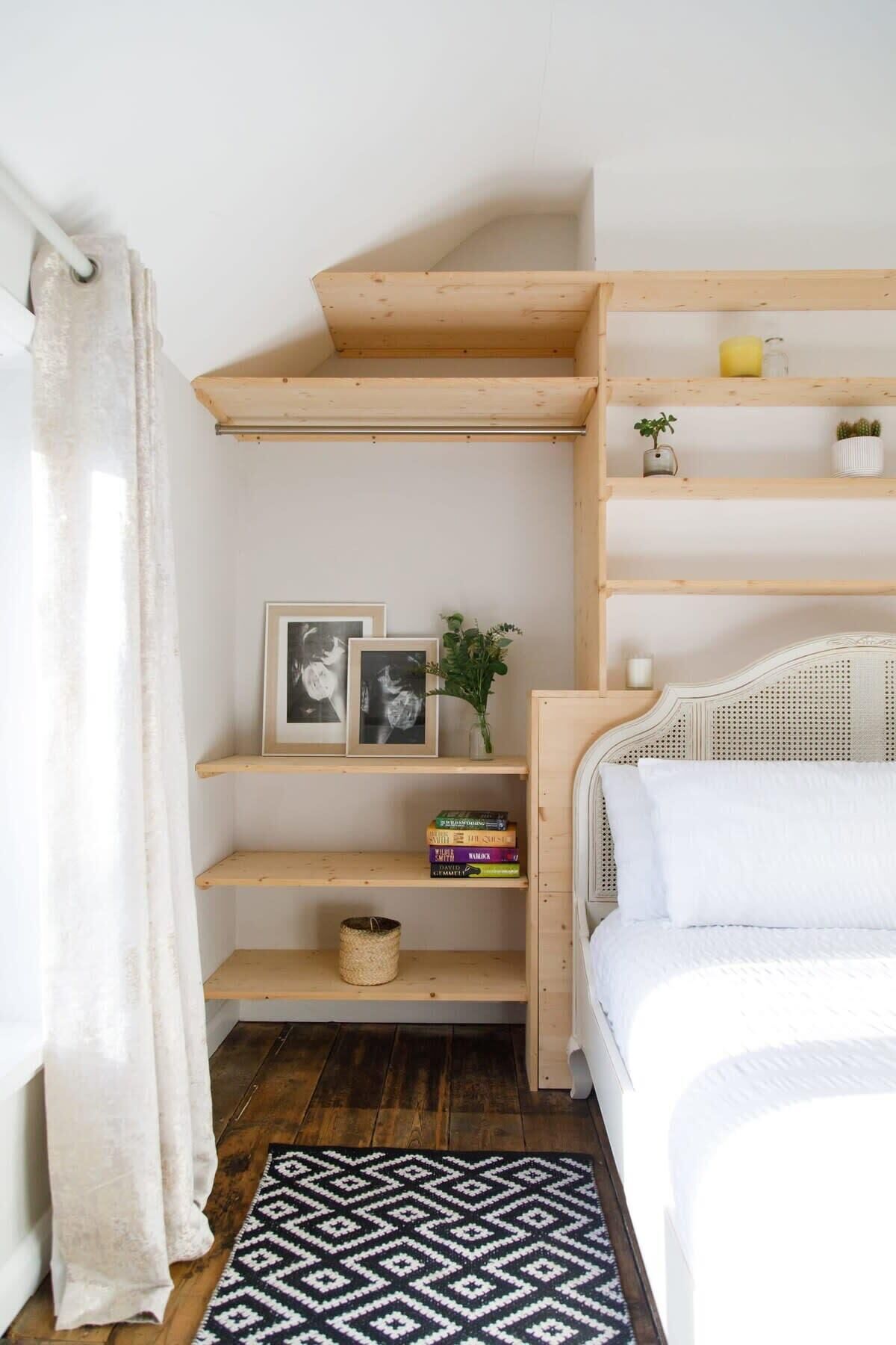 A bedroom with a bed, a wooden shelf unit, a black and white patterned rug, and a white curtain.