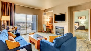 Habitación de hotel con un sofá grande, una mesa de centro, televisión, chimenea y balcón con vistas.