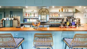 A bar area with a wooden counter, bar stools, and a variety of bottles and glasses. - Five-bedroom home steps from West Wittering beach (West Wittering)