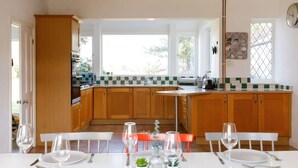 A modern kitchen with wooden cabinets, a central island, and a dining area with a white table set for four. - Five-bedroom home steps from West Wittering beach (West Wittering)