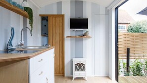 Una cocina moderna con encimera de madera, lavaplatos integrado, un armario blanco, un televisor montado en la pared y un mueble blanco con detalles decorativos.
