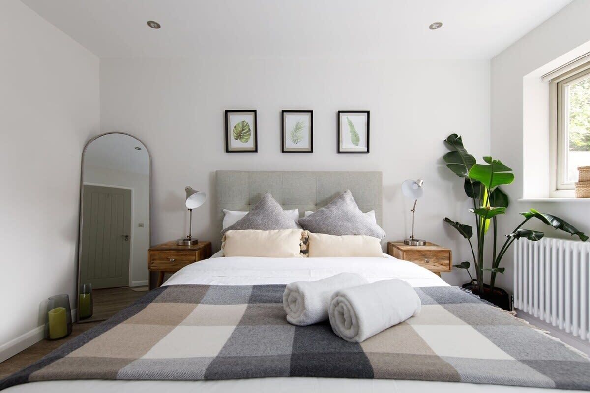 A modern bedroom with a large bed, a headboard, bedside tables, a mirror, and framed botanical prints on the wall.