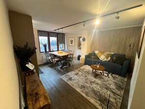 A modern living room with a blue sofa, a wooden coffee table, and a dining area with a wooden table and chairs. - Gemütliche Ferienwohnung in Stadtnähe (Oldenburg)