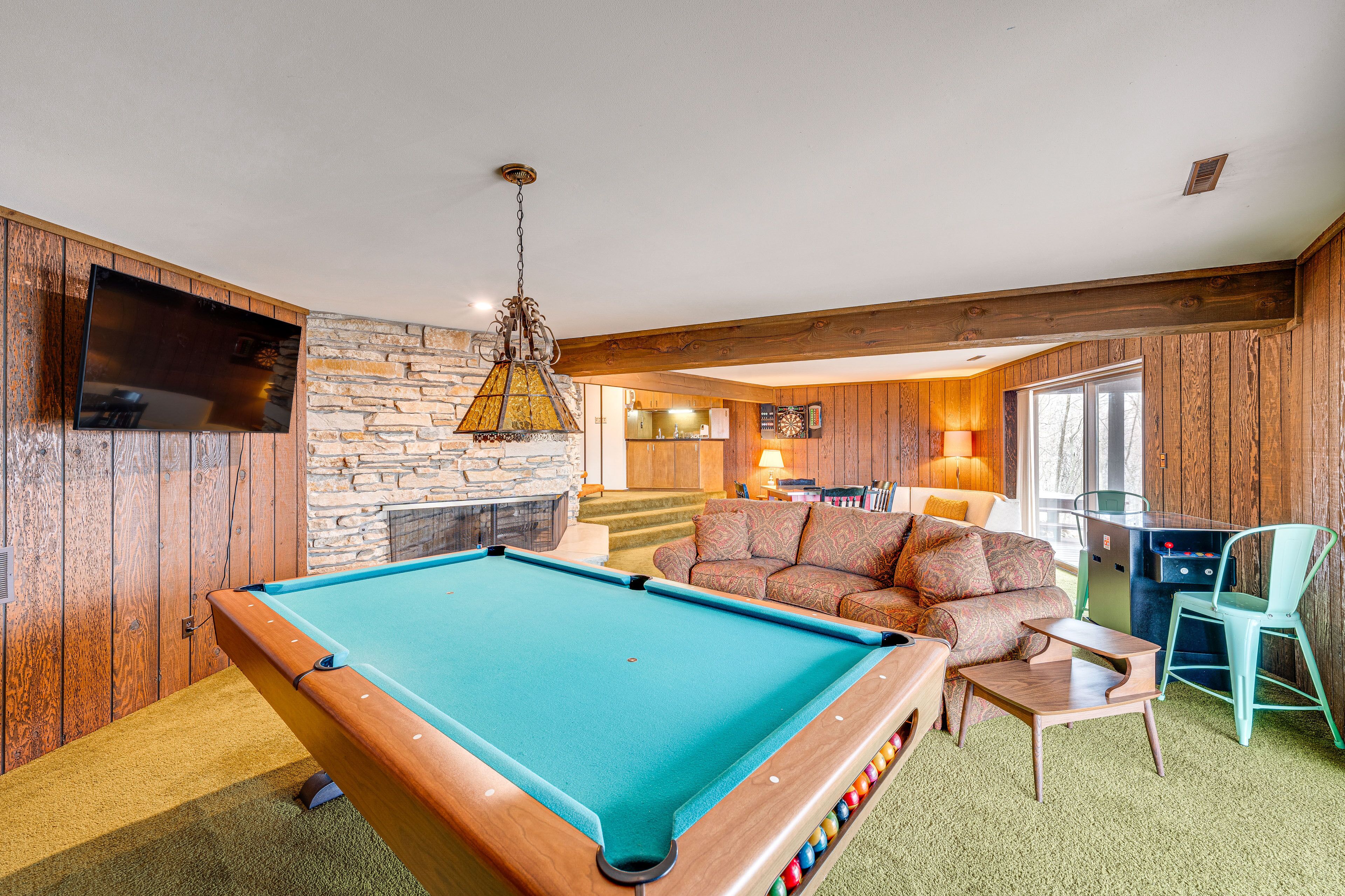 A pool table in a room with wooden walls, a stone fireplace, and a sofa.