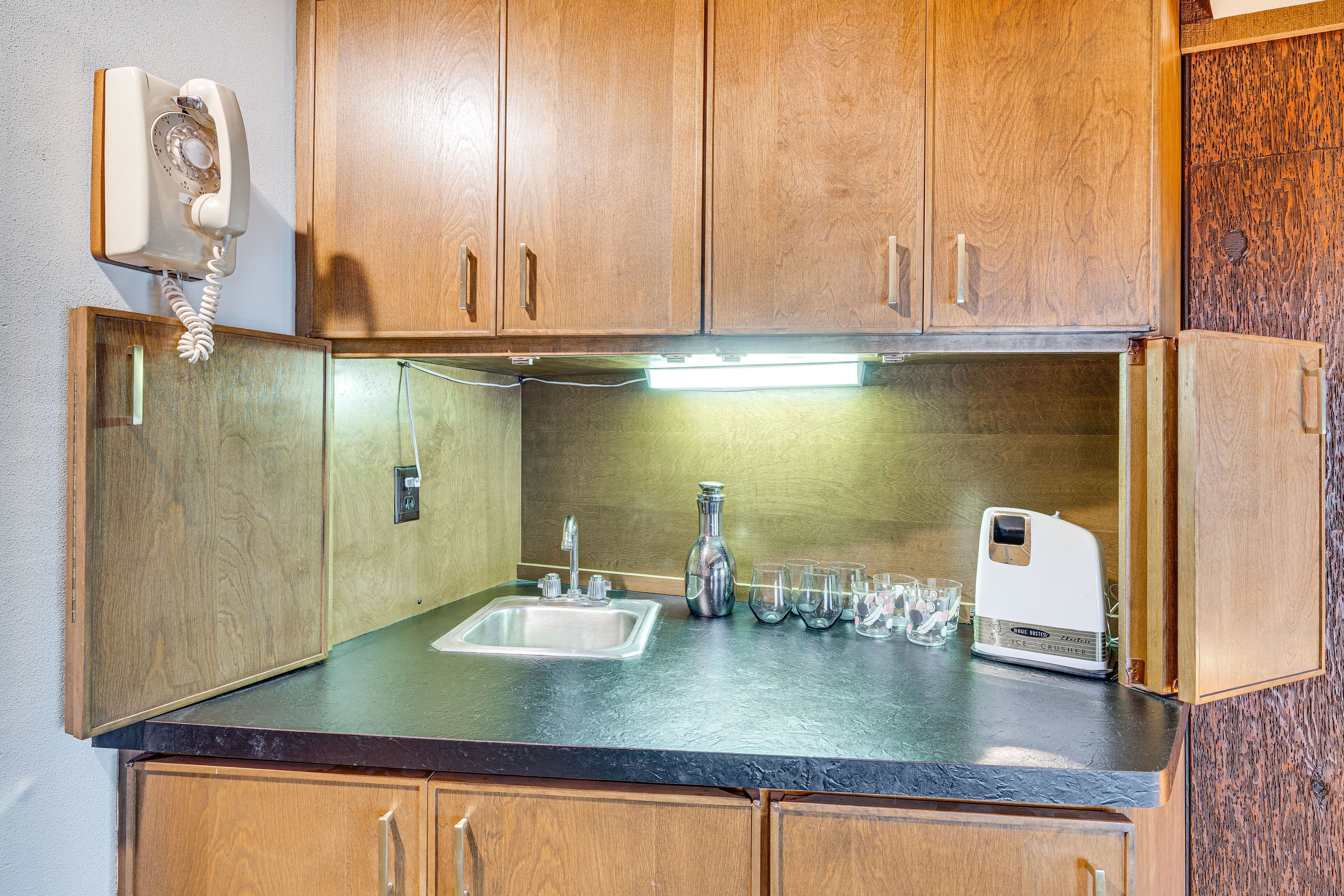 A compact kitchen with wooden cabinets, a sink, a radio, and a few glasses.