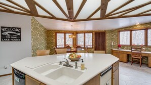 A kitchen with a large island, wooden beams, and a view of trees through windows. - Eclectic Hubertus Home w/ Game Room & Fire Pit! (Hubertus)