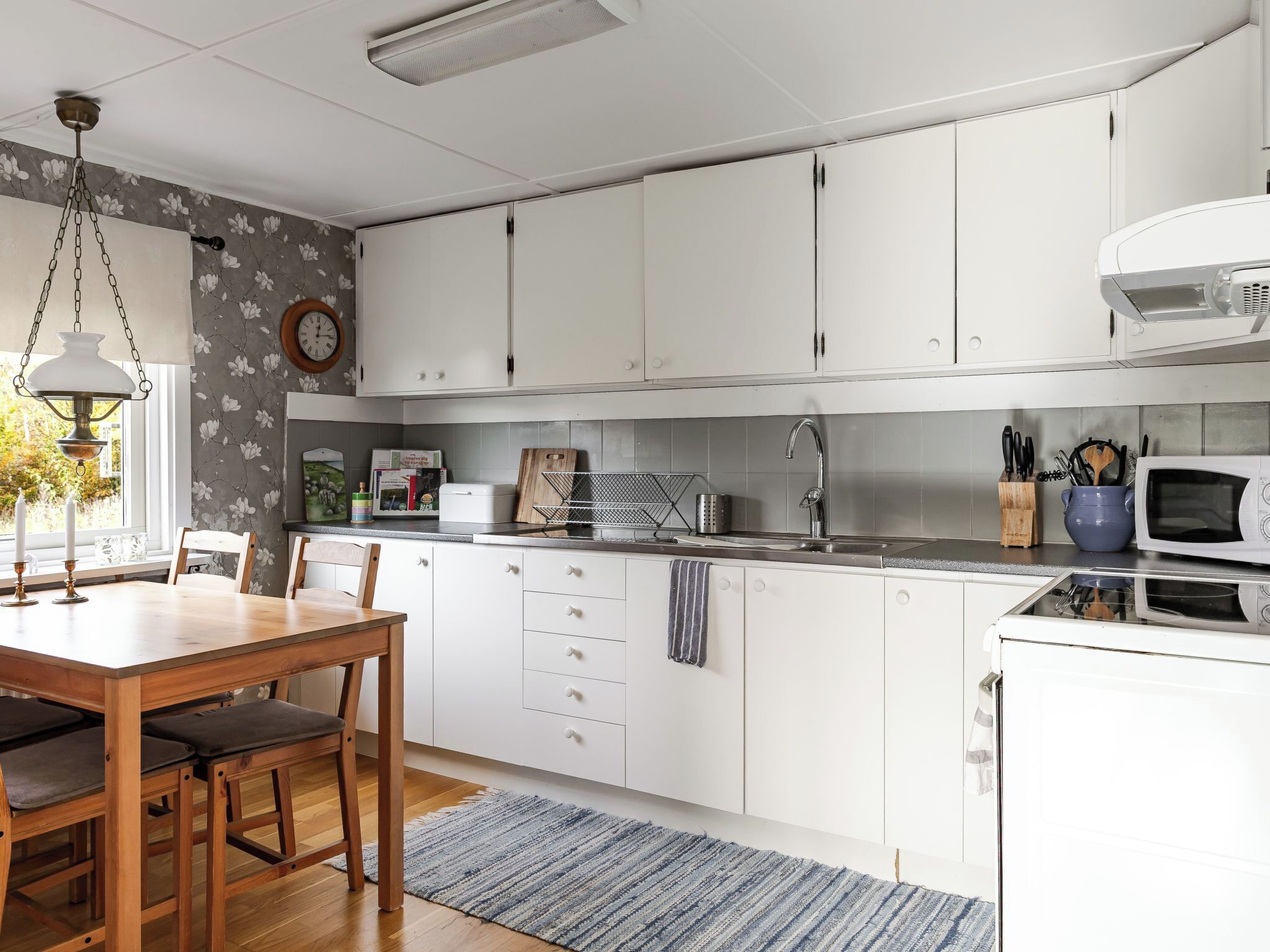 A modern kitchen with white cabinets, a wooden dining table, and a blue rug.