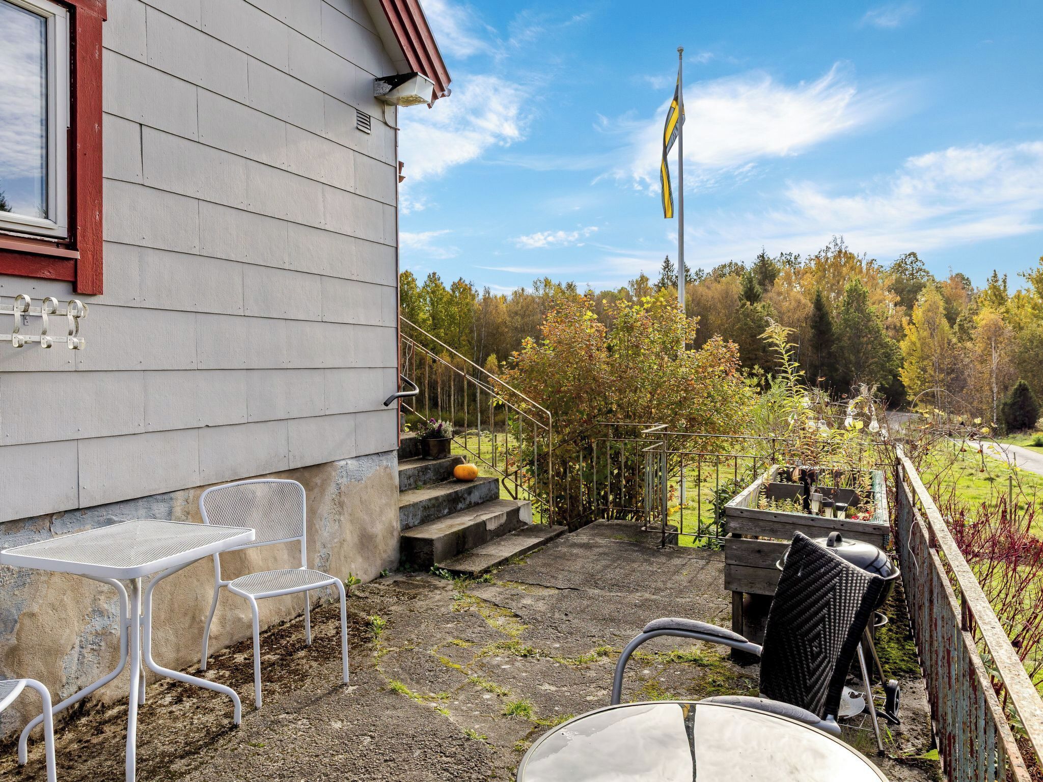 Eine Terrasse mit Sitzgelegenheit, einer Fahnenmast und Blick auf einen bewaldeten Bereich.