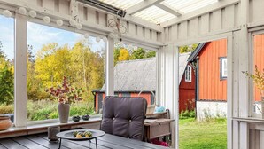 En overdækket terrasse med et bord, en stol og plantekrukker.