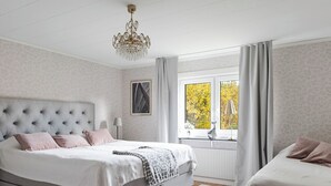 Et soveværelse med en stor seng, en mindre sofa, en lysekrone, et vindue med gardiner og en radiator.