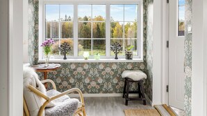 A cozy room with a large window, a wooden chair, a small stool, and a table with a lamp and flowers. - Skjutsmåla by Interhome (Olofström)