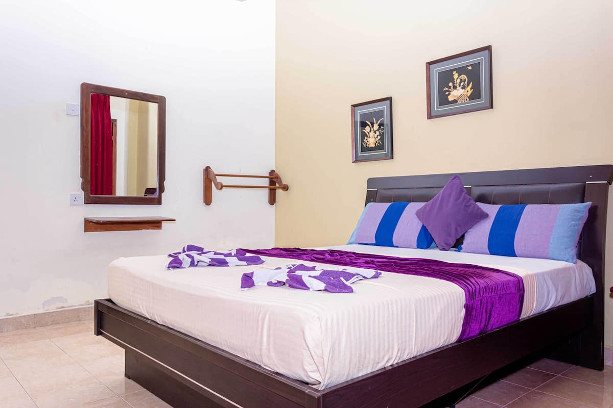 A neatly made bed with a purple and white striped blanket, a wooden headboard, and two framed pictures on the wall.