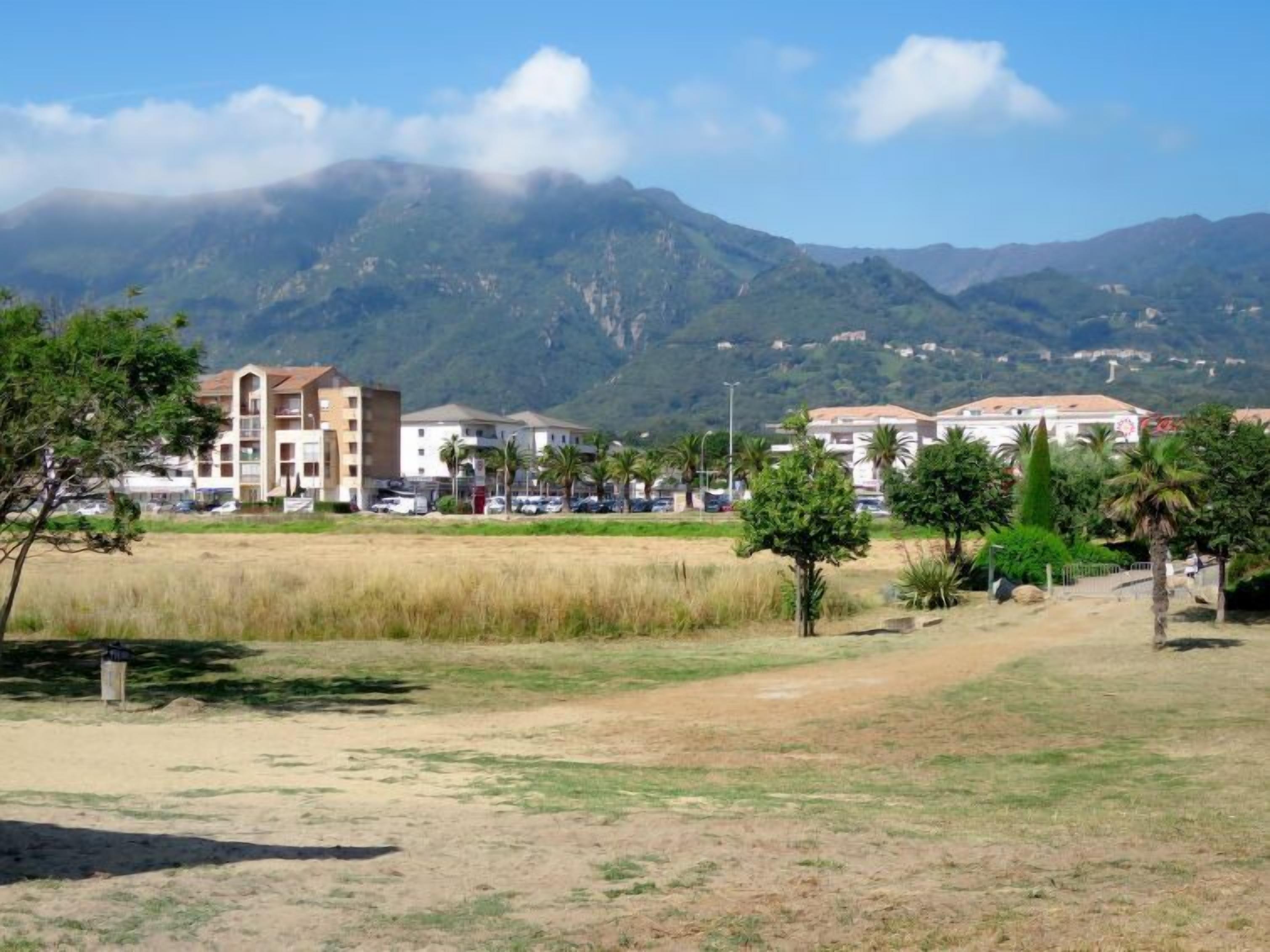 A residential area with buildings, a grassy field, and mountains in the background.