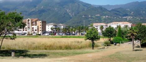 A residential area with buildings, a grassy field, and mountains in the background.