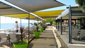 A seaside restaurant with outdoor seating, potted plants, and a view of the ocean.