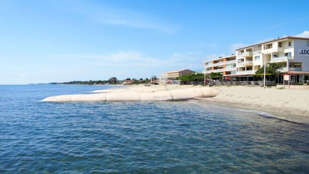 A coastal hotel with clear blue waters, a sandy beach, and a white building with balconies.