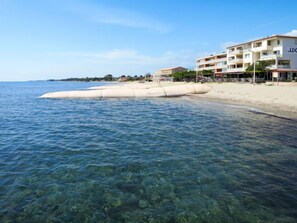 A coastal hotel with clear blue waters, a sandy beach, and a white building with balconies.