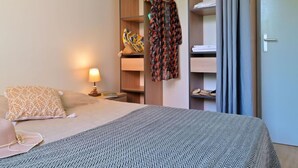 A bedroom with a bed, a nightstand, a lamp, a wardrobe, and a mirror.