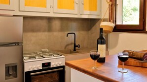 A kitchen with white cabinets, a gas stove, an oven, a sink, and a window with a view of greenery.