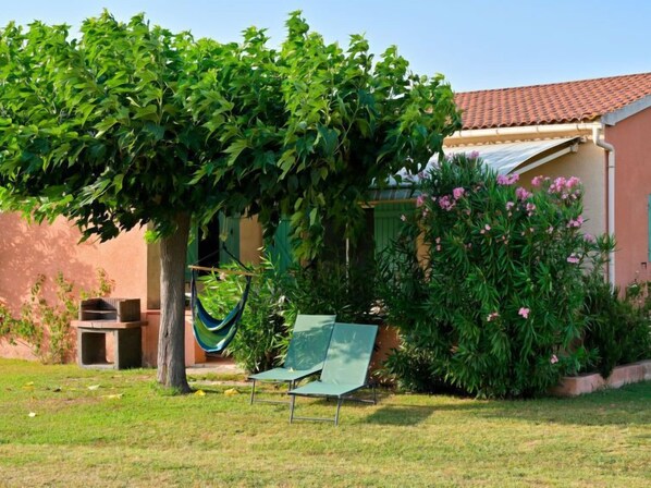 A garden with a hammock, a chair, and a house with a red roof.