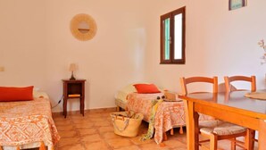 A room with a bed, a small table, a chair, a window, and a wall-mounted air conditioner.