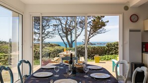 Uma sala de jantar com uma mesa posta para quatro pessoas, com vista para o mar e árvores.