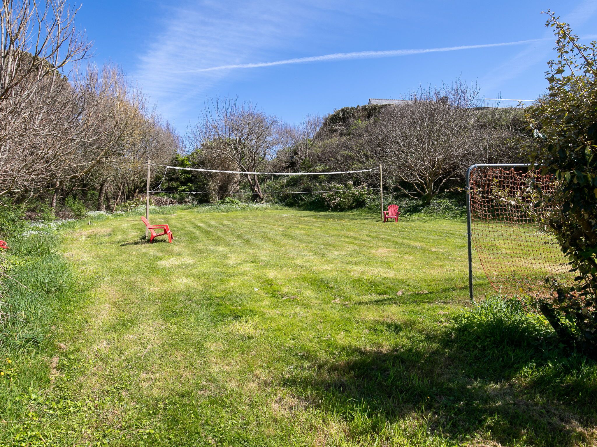 A grassy outdoor area with a volleyball net, a red chair, and a wooden bench.