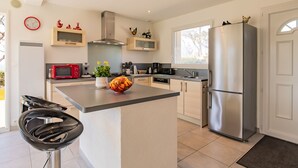 Cozinha moderna com ilha central, eletrodomésticos de aço inoxidável e área de jantar com uma cadeira preta.