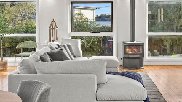 En moderne stue med en grå sofa, et rundt træbord og en pejs.