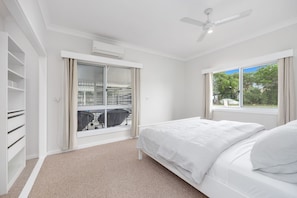 Un dormitorio con cama, ventana con vistas a árboles, ventilador de techo y puerta corrediza que da a un balcón.
