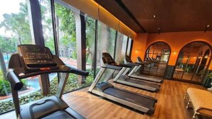 A gym with treadmills aligned in rows, large windows, and a view of greenery outside.