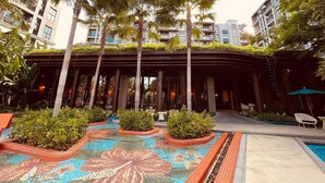 A hotel courtyard with a pool, palm trees, and a covered seating area.