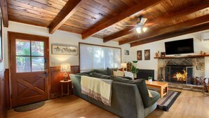 Un salon chaleureux avec une cheminée, des poutres apparentes en bois au plafond, un canapé et un téléviseur.