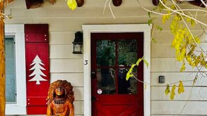 Une maison en bois avec une porte rouge et une statue en bois représentant une personne.
