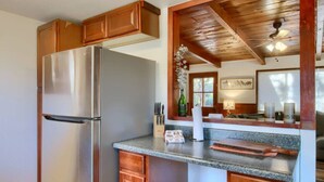 Une cuisine équipée d’un réfrigérateur en acier inoxydable, de meubles en bois, de plans de travail en granit et d’une fenêtre agrémentée d’objets décoratifs.