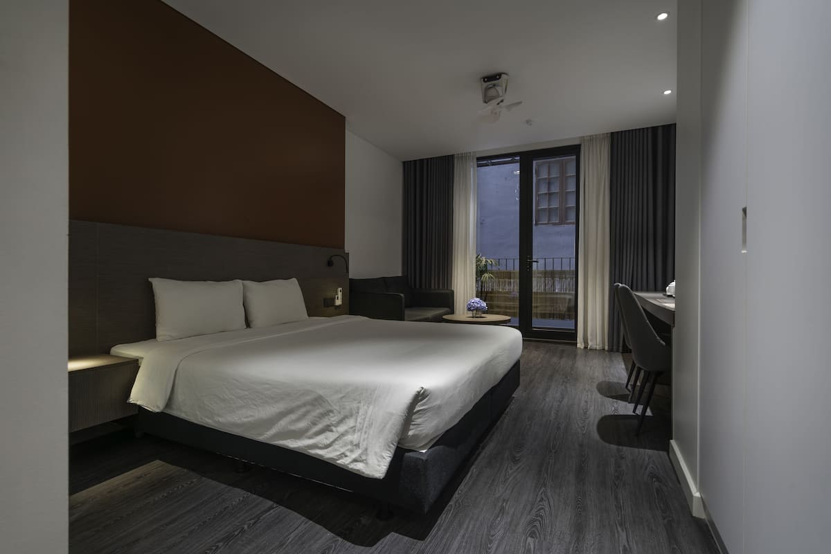 Quarto de hotel moderno com uma cama grande, uma escrivaninha e uma varanda com cortinas.