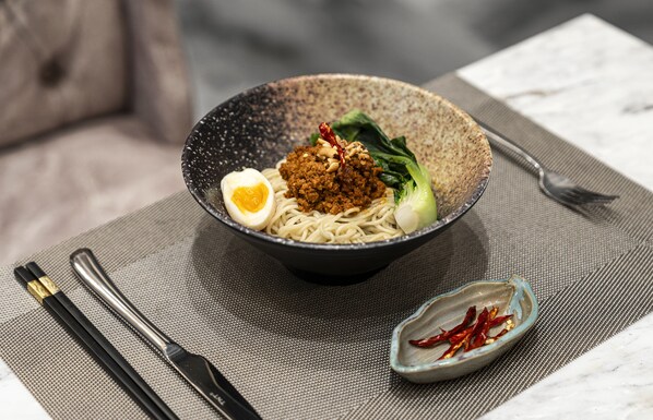 Un tazón de fideos con huevo cocido, carne y verduras sobre un tapete texturizado.