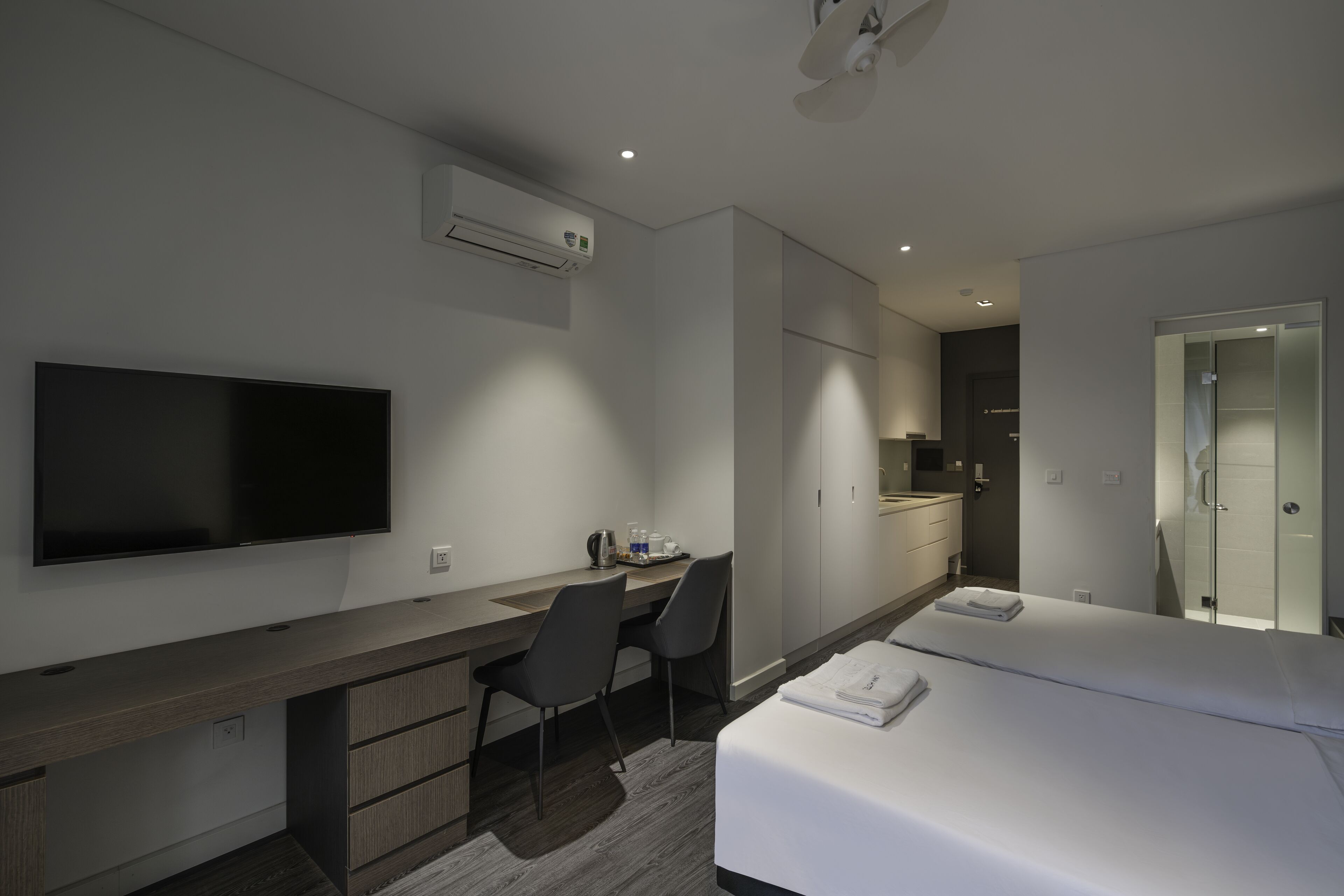 Ett modernt hotellrum med en platt-TV, ett skrivbord med två stolar, en säng med ett vitt överkast och en rymlig klädkammare.
