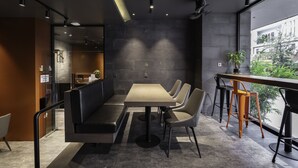 Un comedor moderno con una mesa larga y varias sillas, una partición de vidrio y vistas a zonas verdes exteriores.