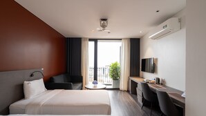 Habitación de hotel con dos camas, un escritorio, una silla, un televisor y un balcón con una planta.